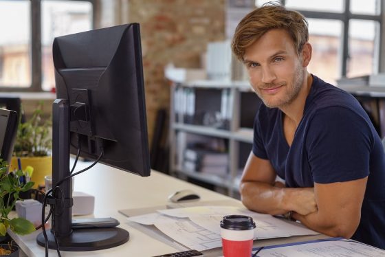 Smilende mand ved sit skrivebord med computer og bilag